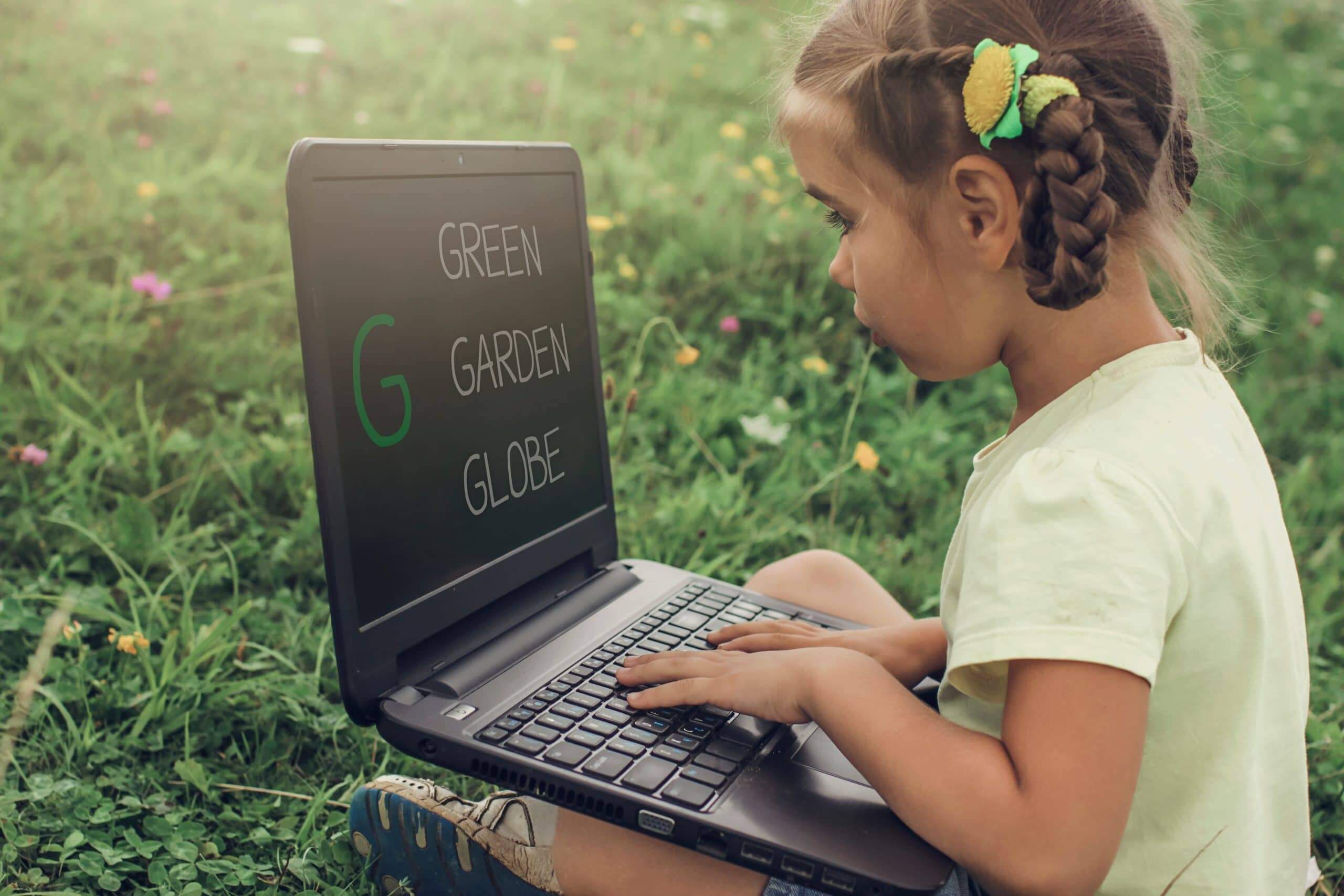 pupil sitting on green grass outdoor and using laptop for distan